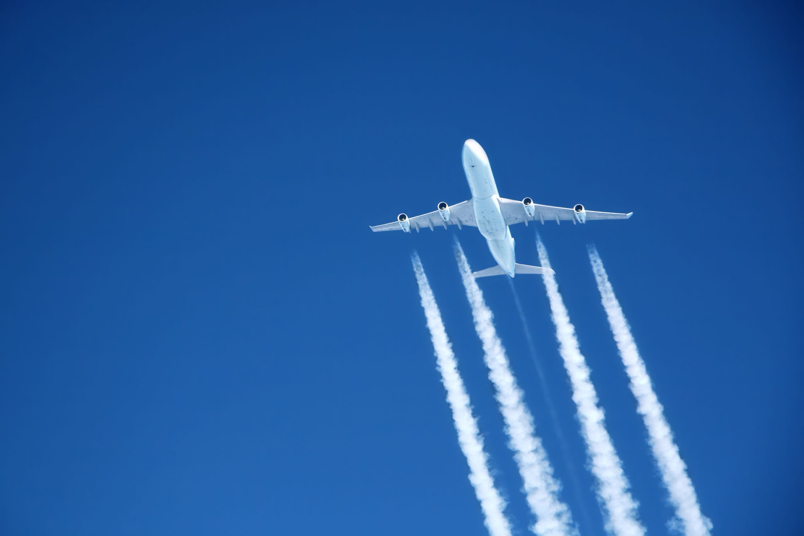 Plane flying through a blue sky casting exhaust fumes behind it