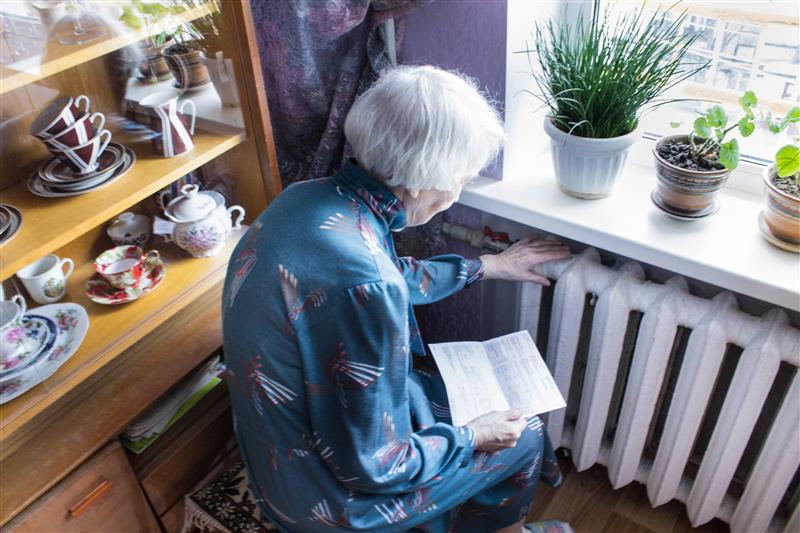 photography of elderly woman holding gas bill in front of heating radiator.