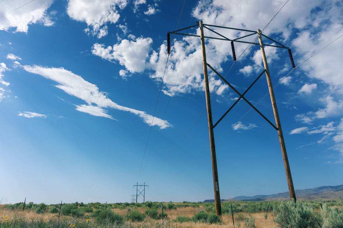 photography of grey electric poles on a field against a blue sky