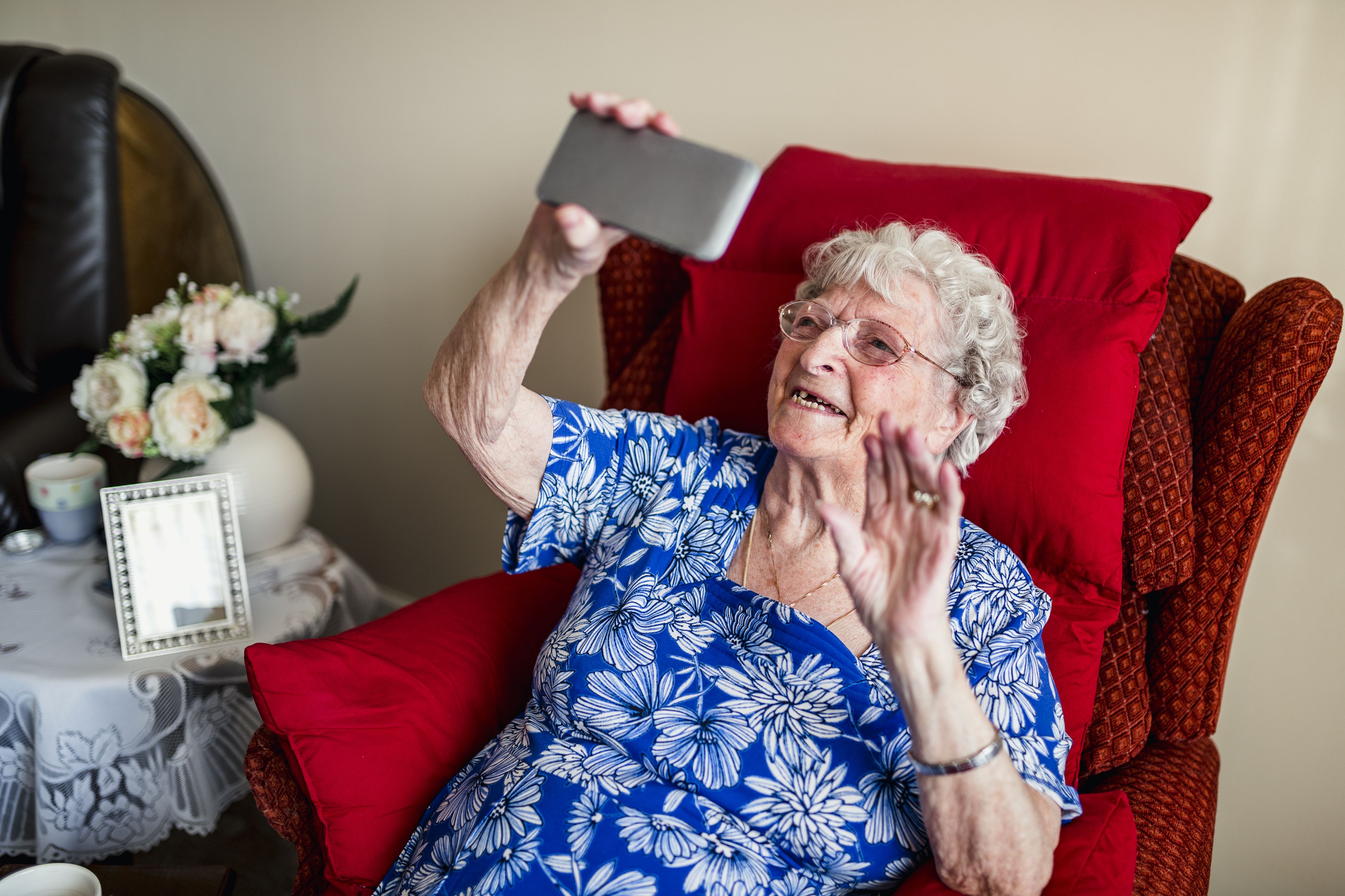 An elderly woman sitting on a chair and doing a video call to relatives on her phone