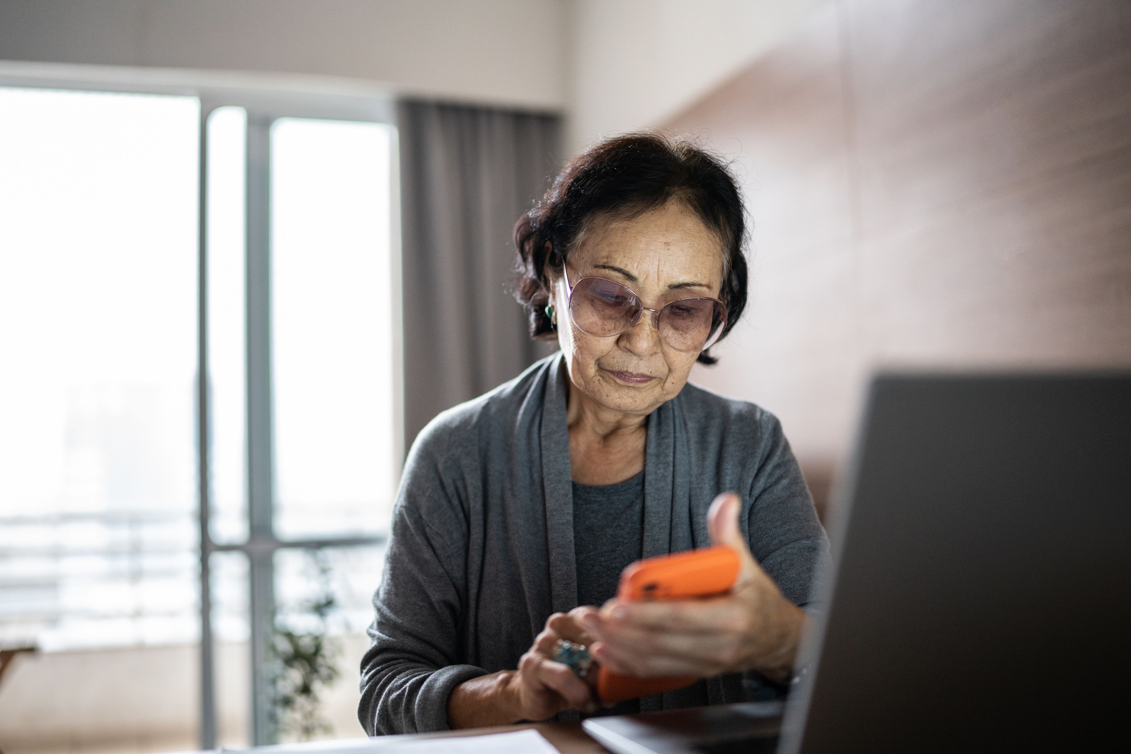 Senior woman paying bills with mobile phone at home