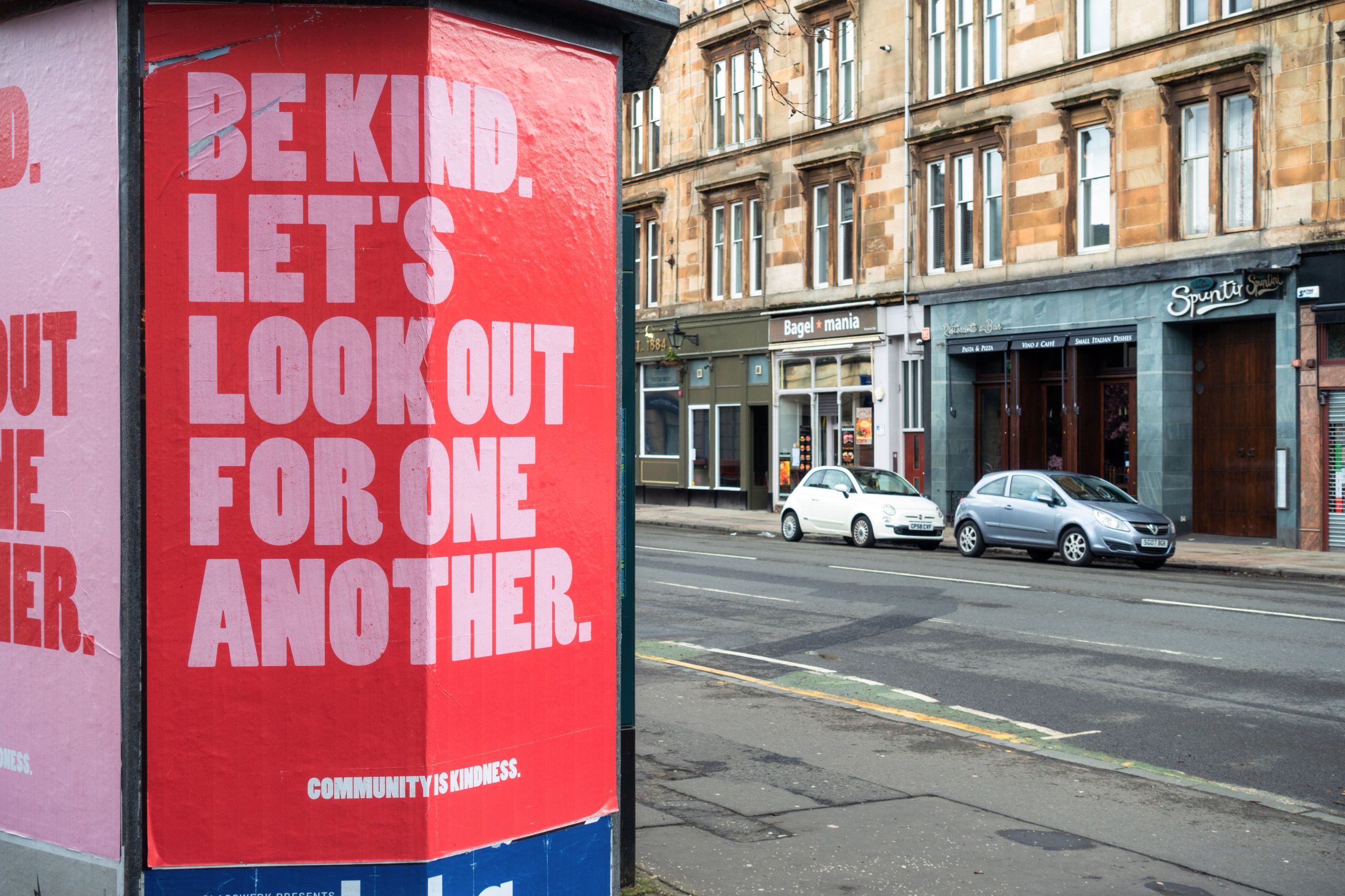 Image of buildings on a road with a sign that reads 'Be kind, let's look out for one another'