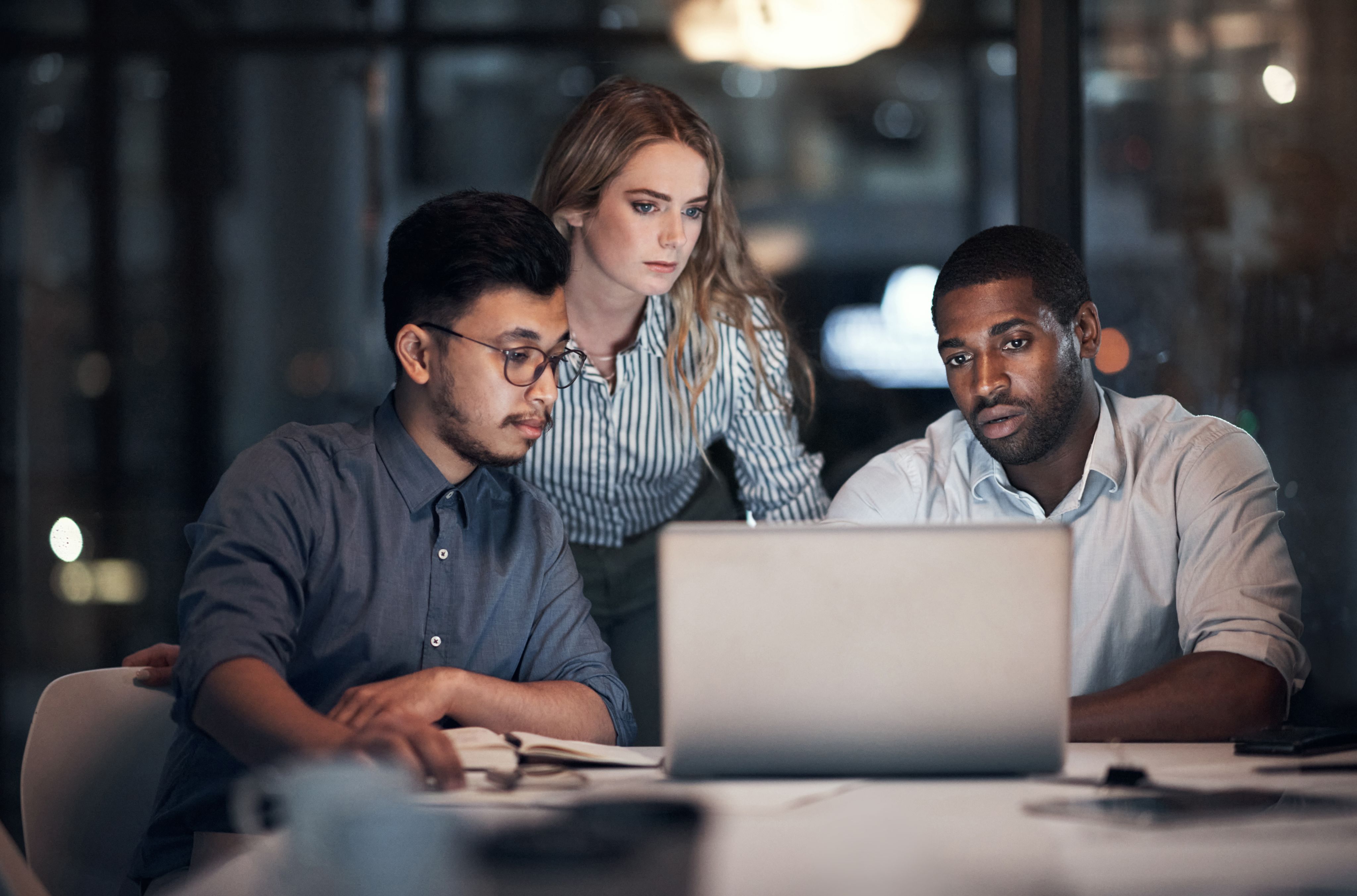 Three people looking at a laptop screen in an office late at night