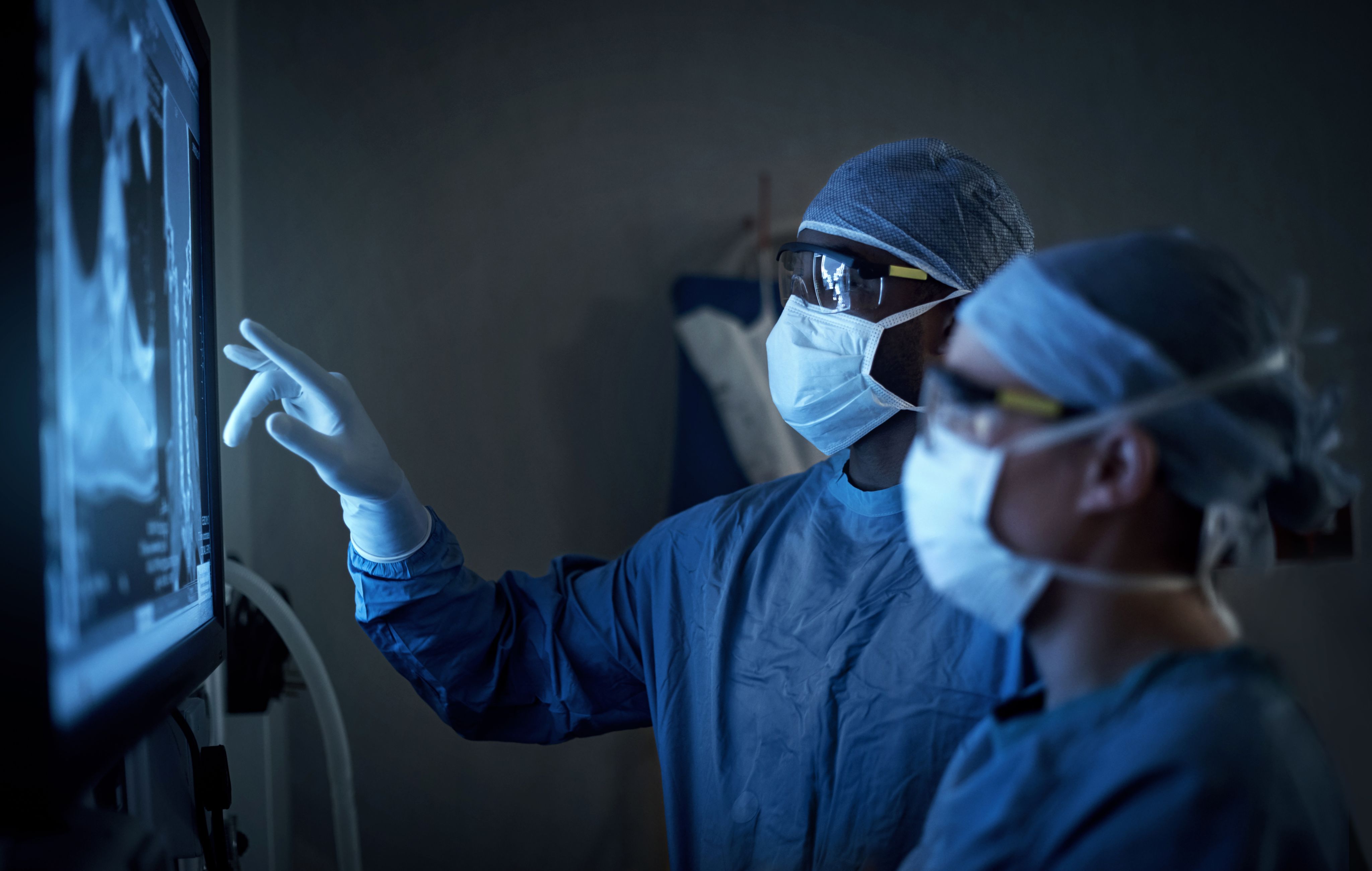 Two surgeons in scrubs looking at a scan on an electronic screen.