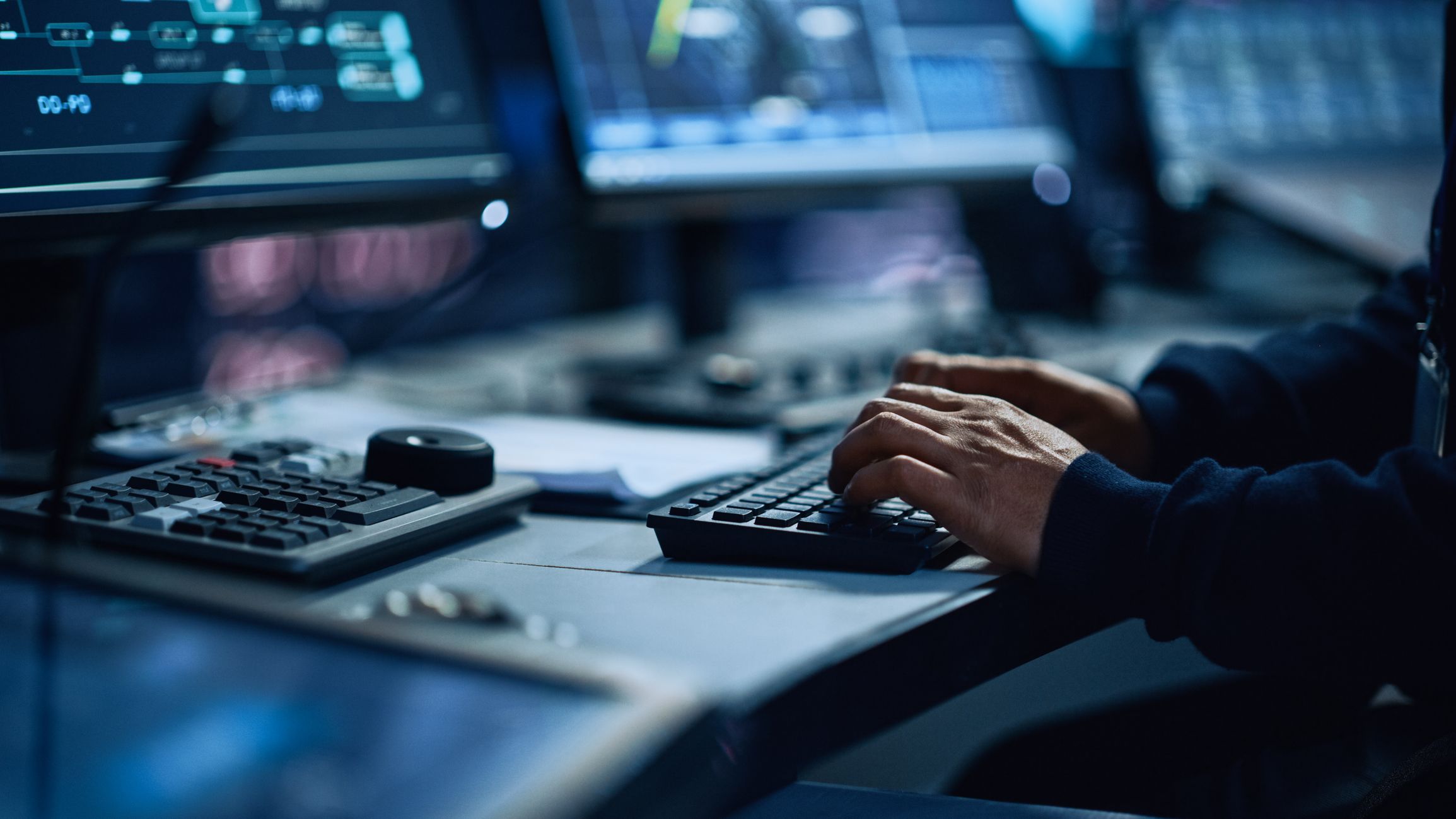 Person typing on a keyboard with multiple computer screens in front of them