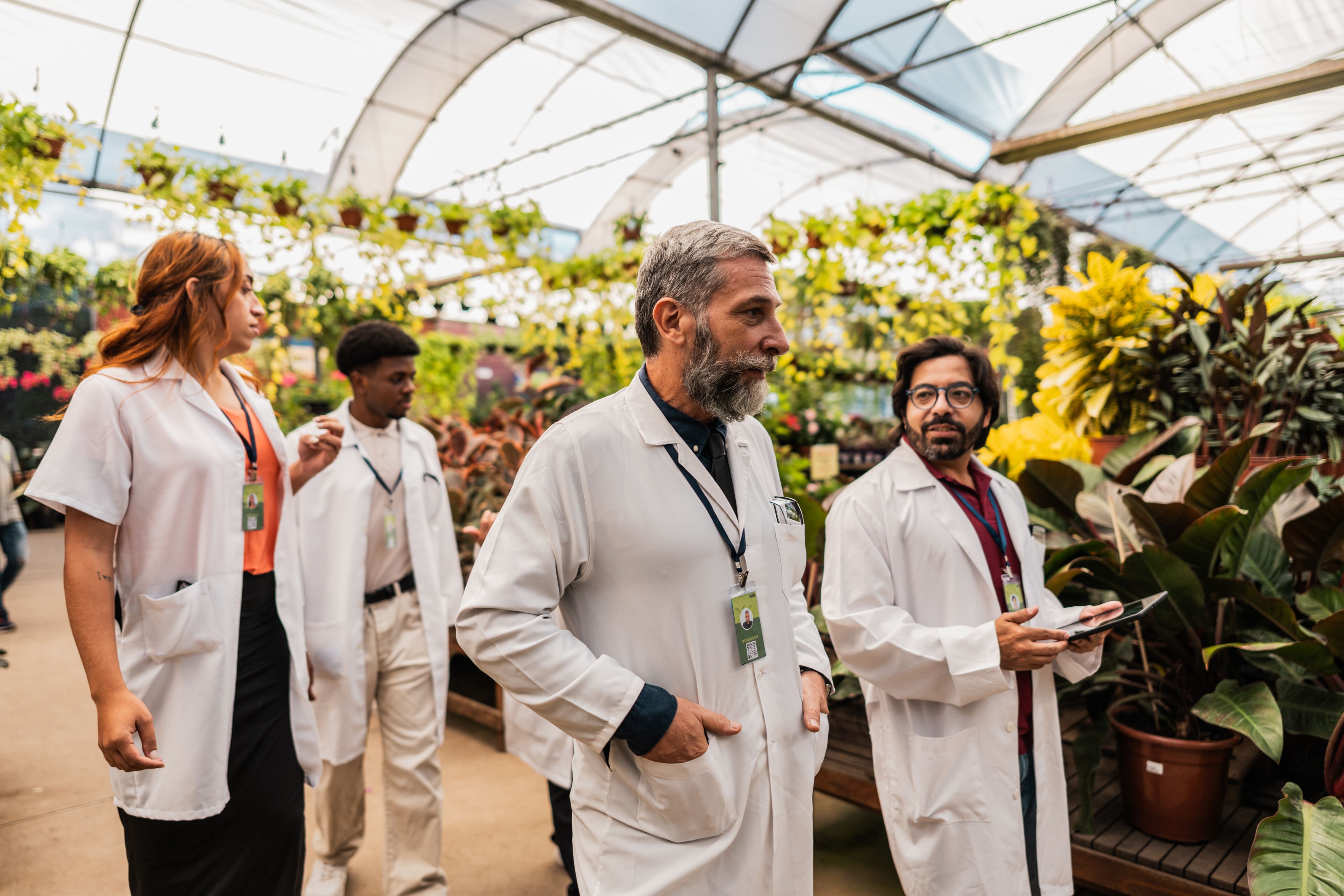 Doctors in white coats walking through a greenhouse. One talking and holding a clipboard.