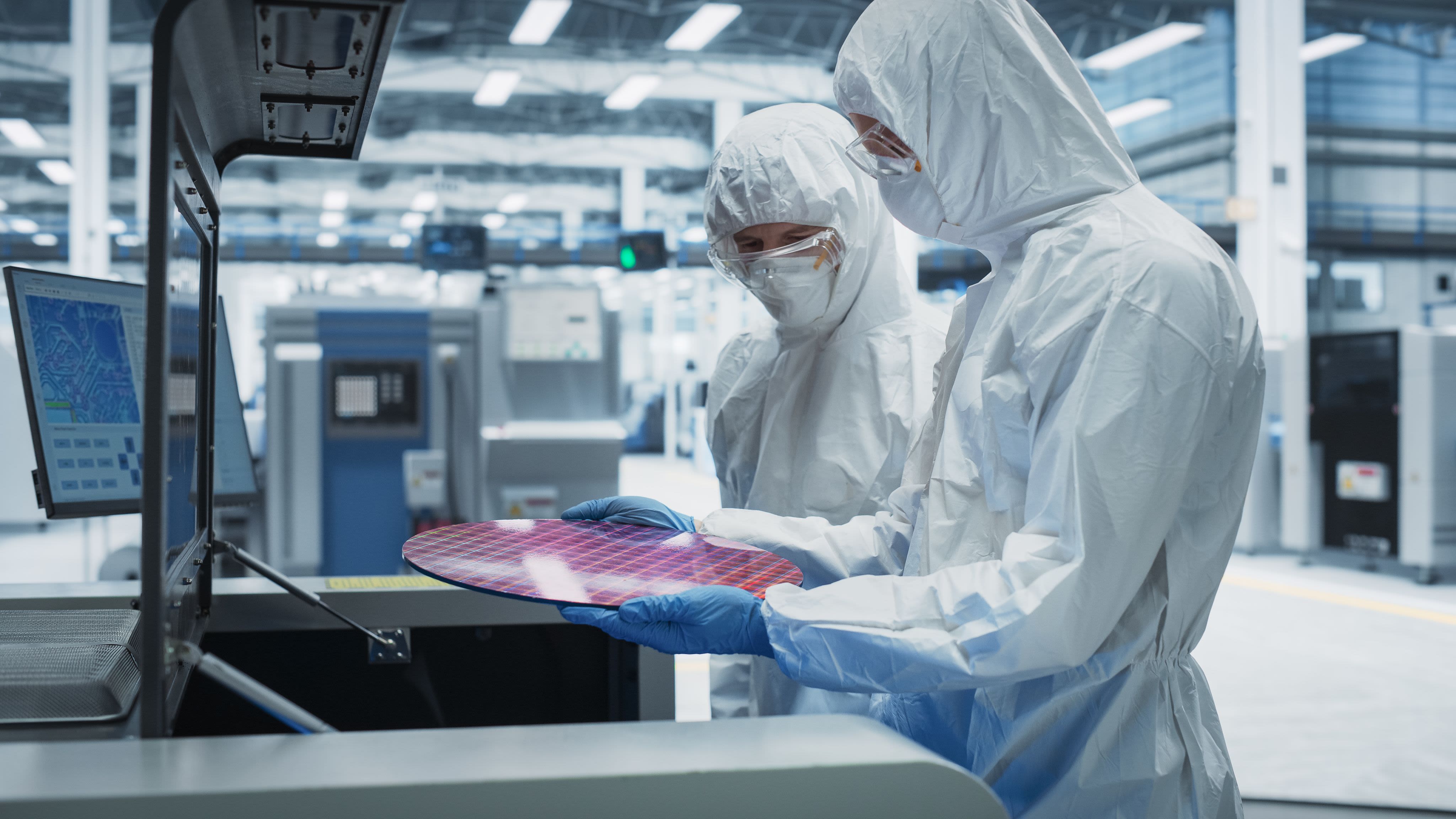 Two scientists in protective clothing looking at a layer of semiconductors in a lab.