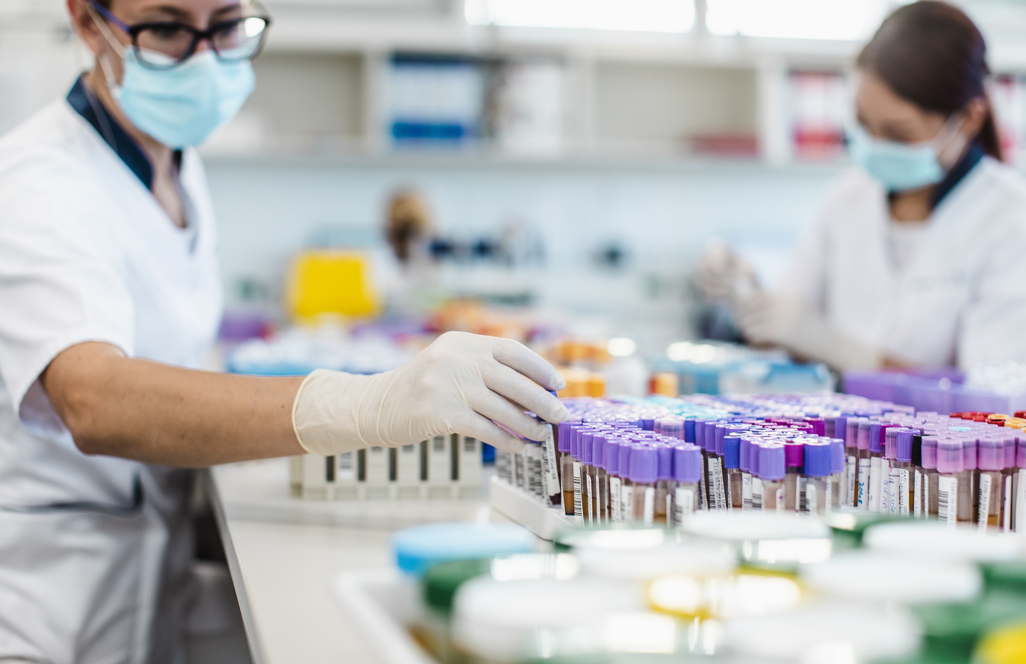 Two women in protective clothing sorting blood samples in test tubes
