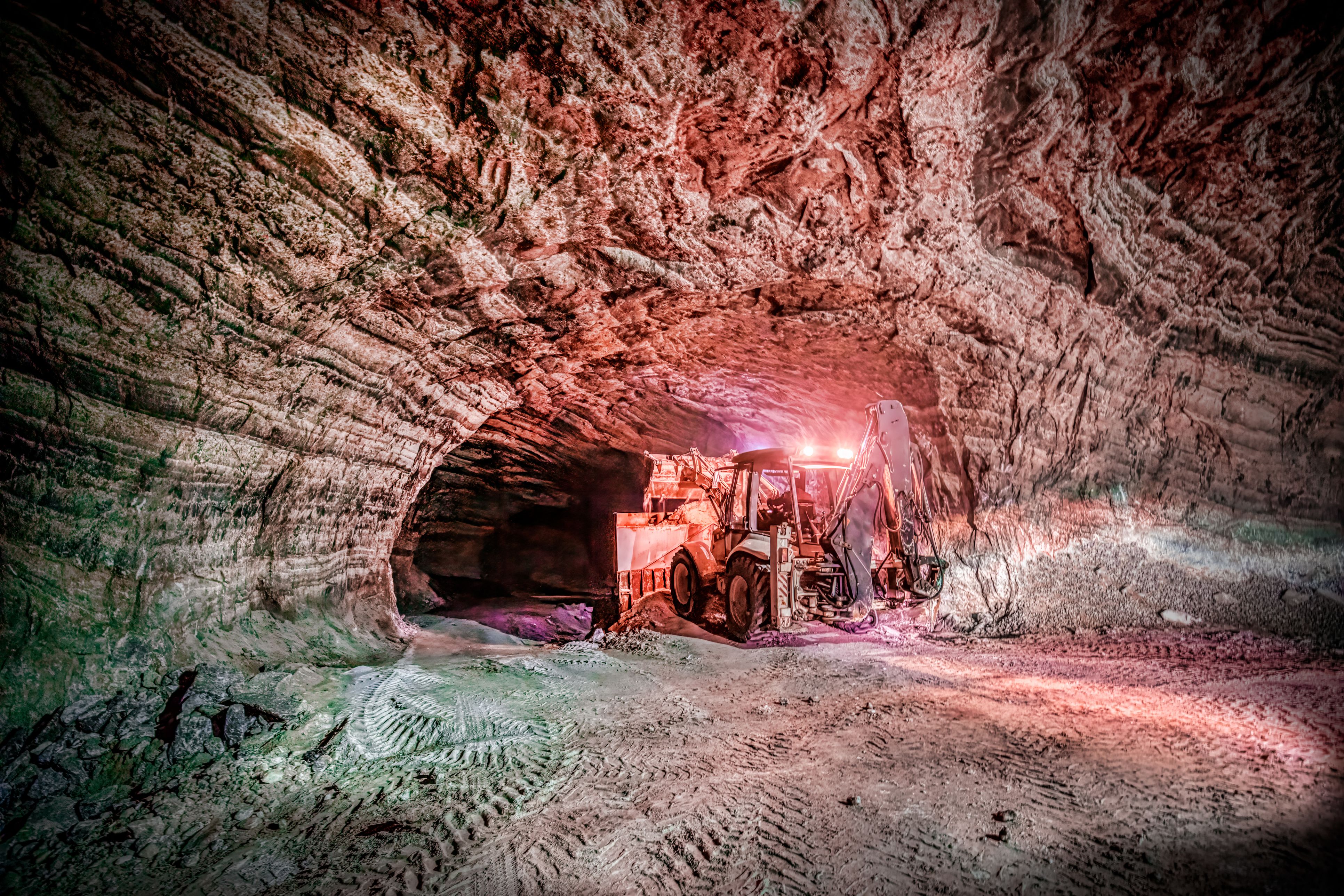 An image of a digger, digging into the earth of an underground mine
