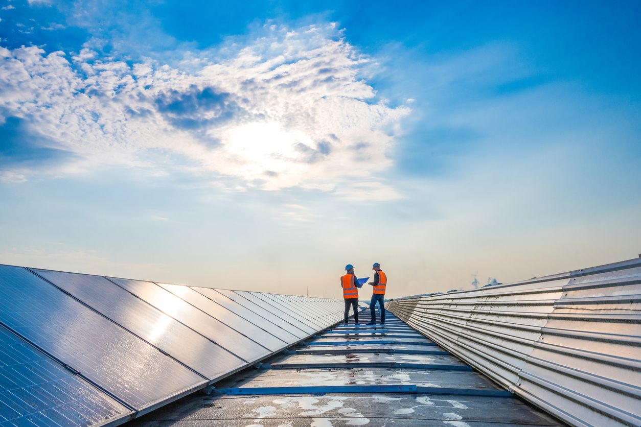 Two people in hi-viz vests standing on some solar panels