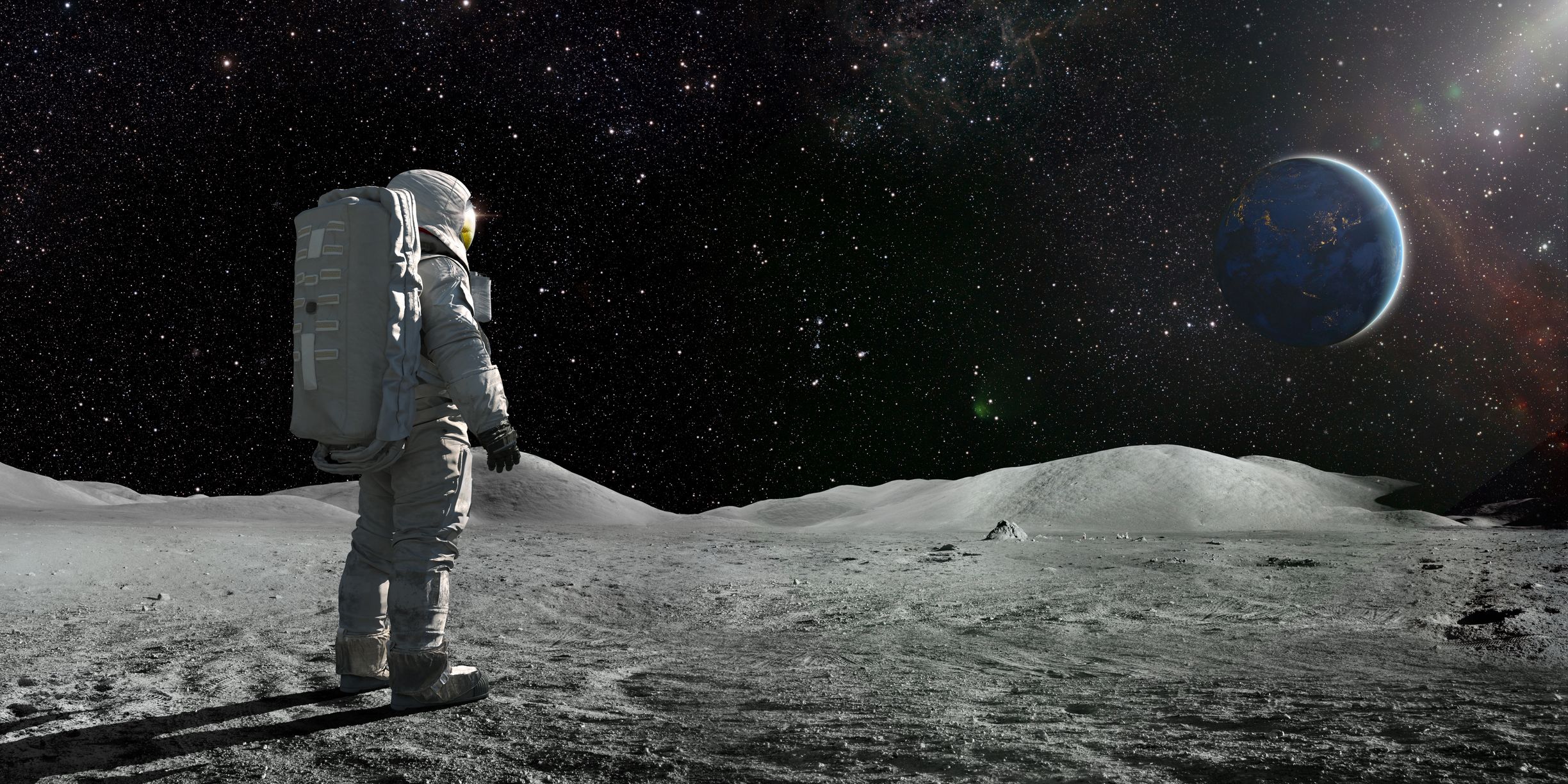 astronaut standing on the moon looking towards a distant earth