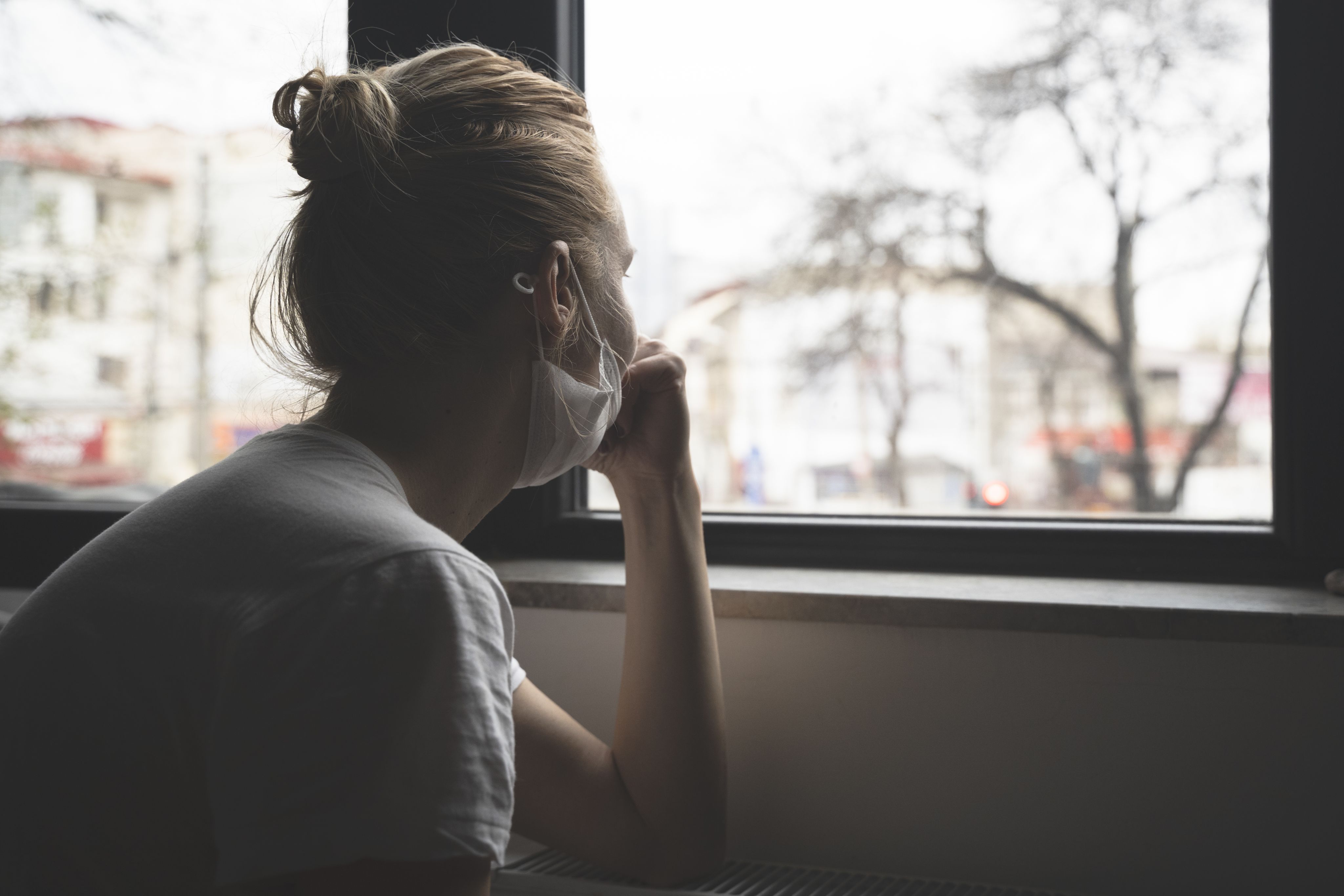 A young woman wearing a facemask looks out of the window
