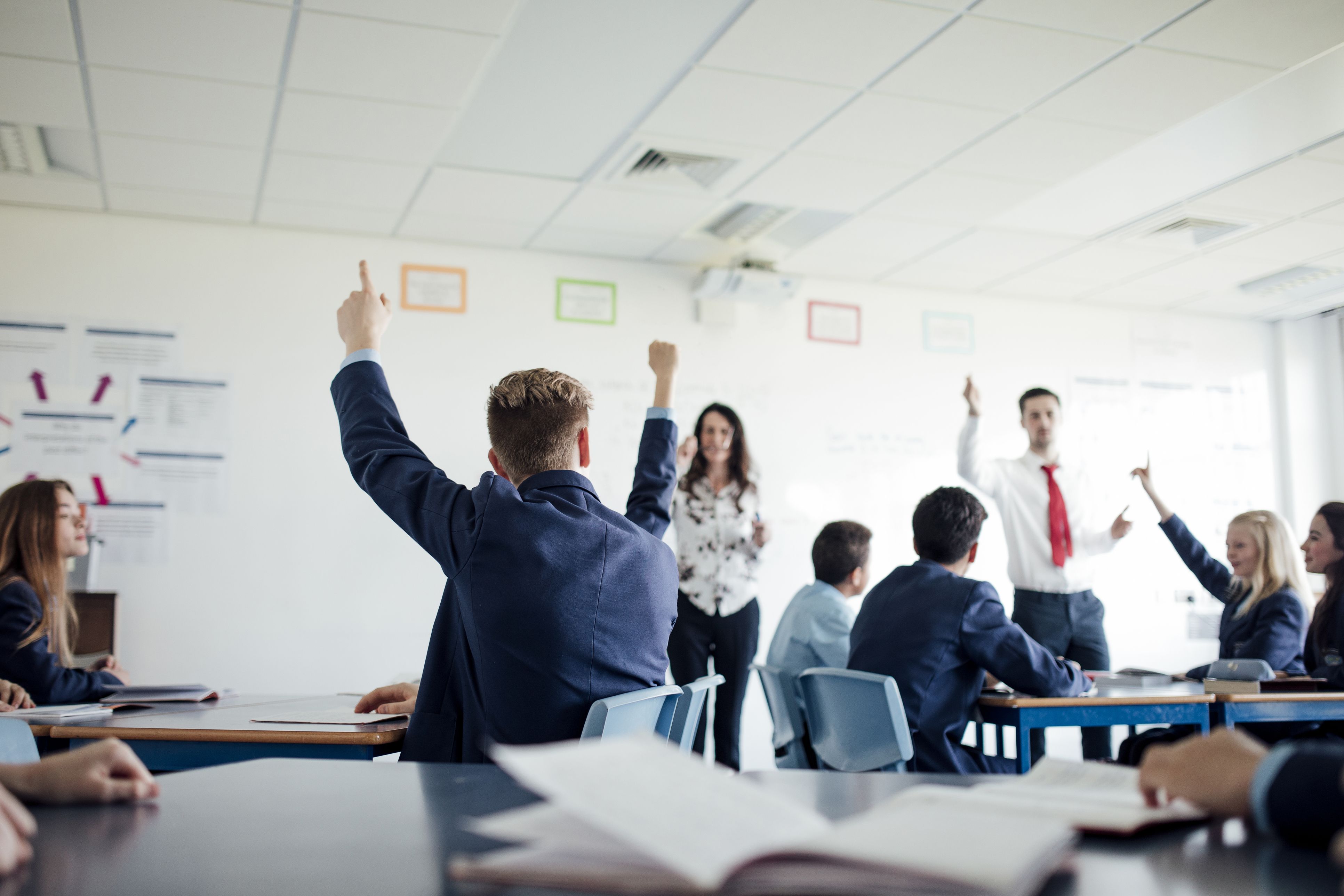 Schoolchildren in uniform raise their hands in class