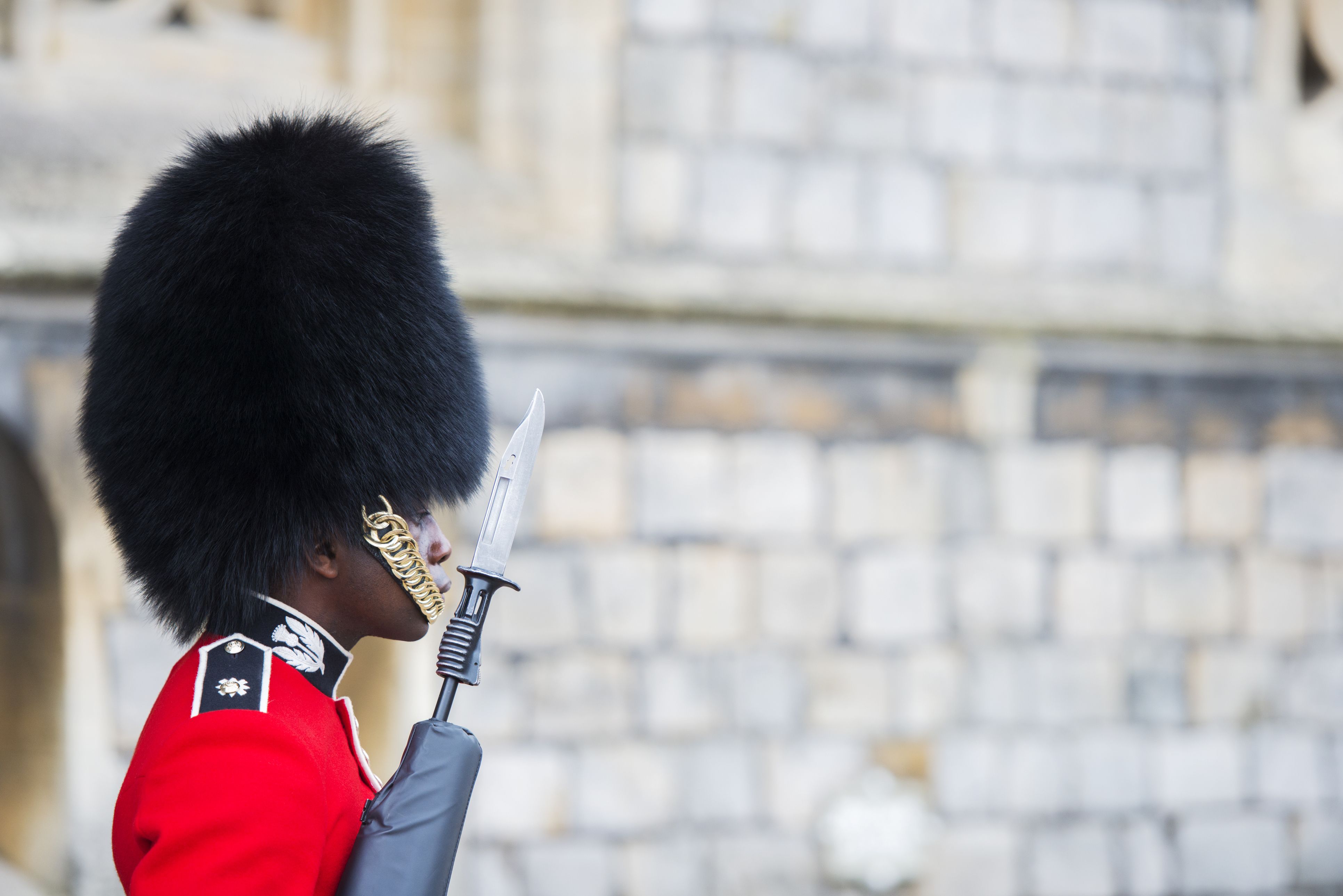 A young Black soldier in ceremonial uniform and bearskin hat stands guard