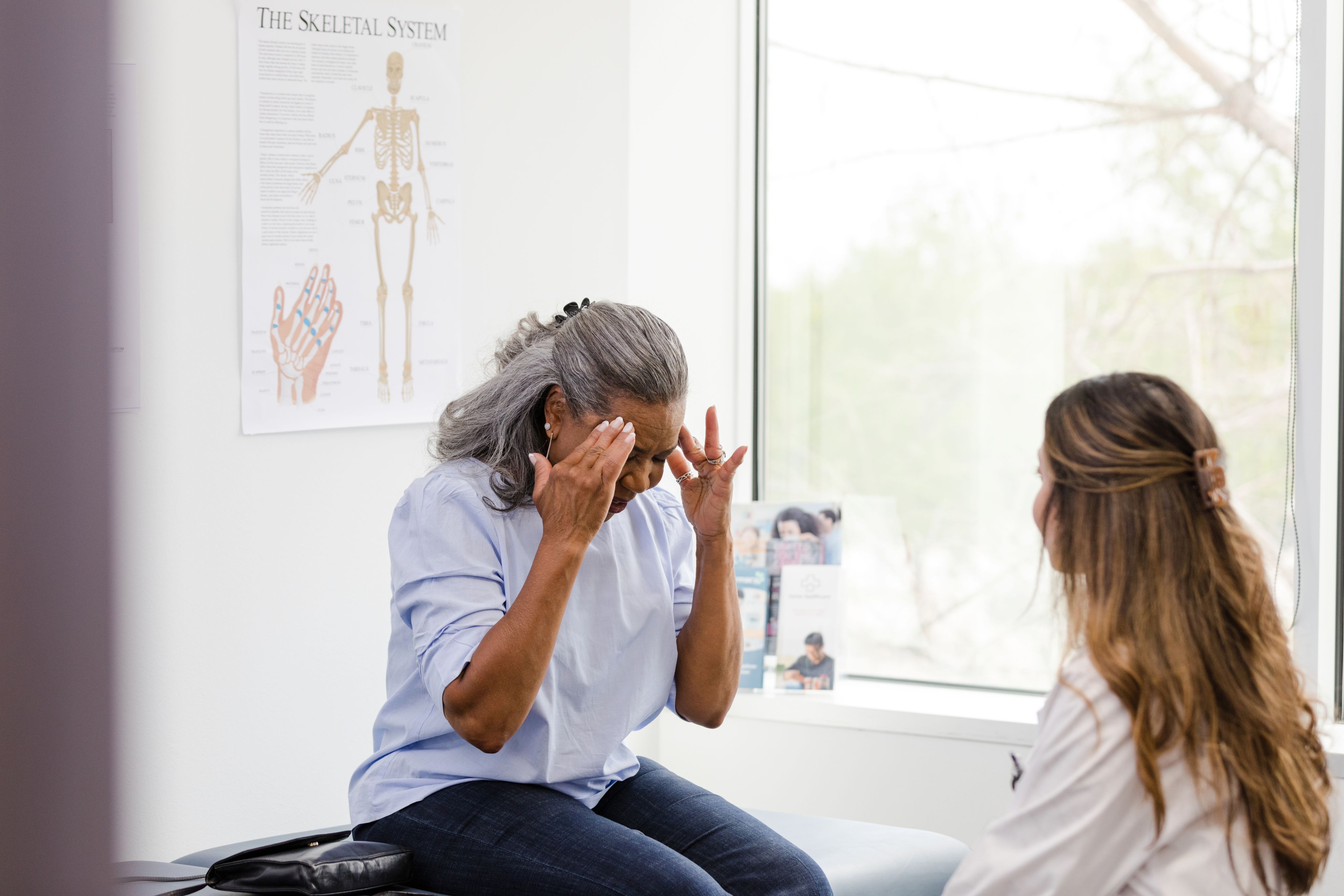 An older patient holding their head while speaking with a medical worker.