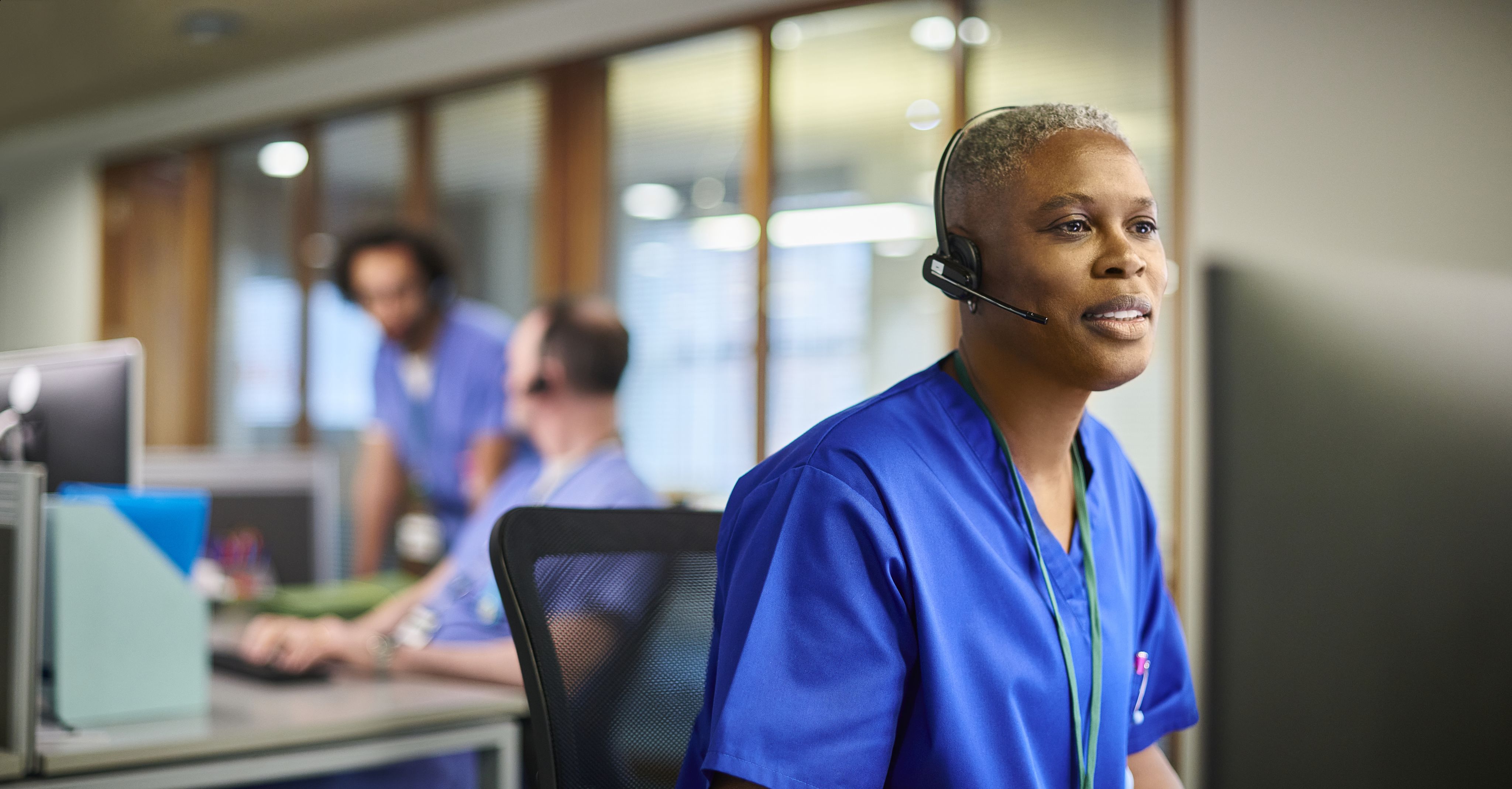 A medical worker sitting at a desk speaking on a headset.