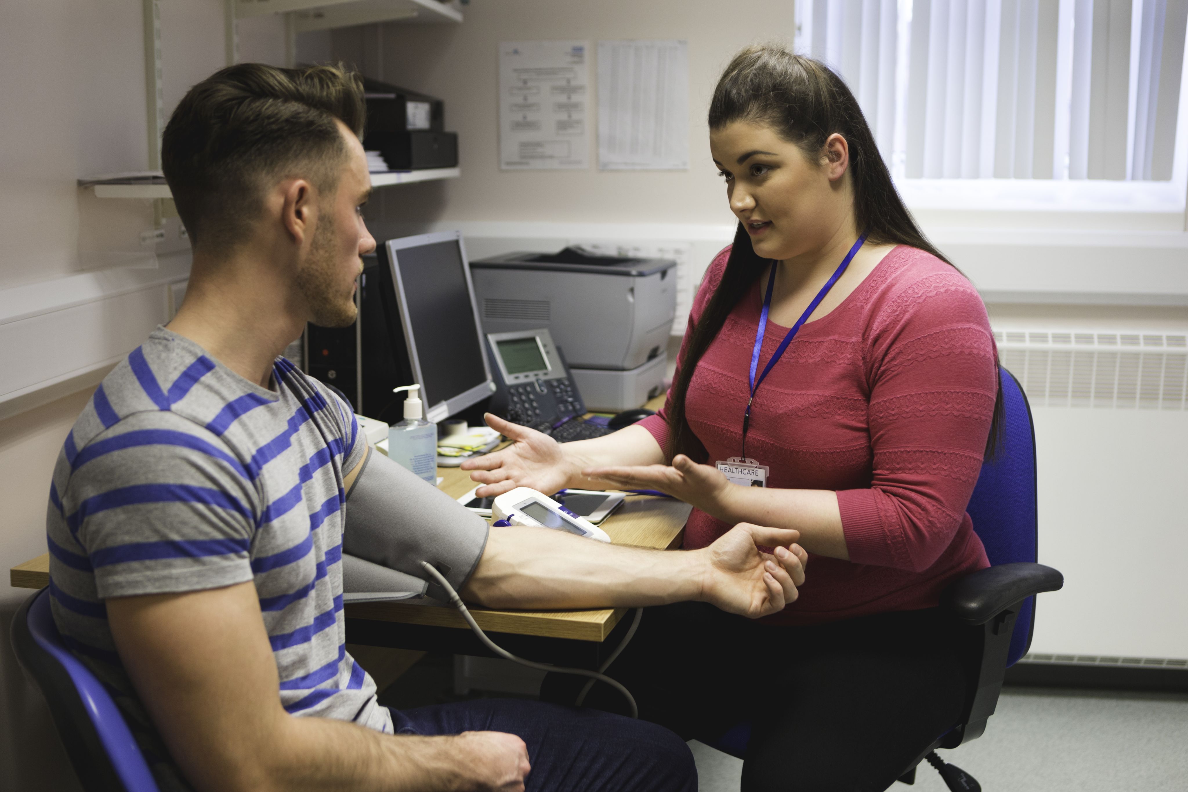 A GP taking the blood pressure of a patient while talking to them.