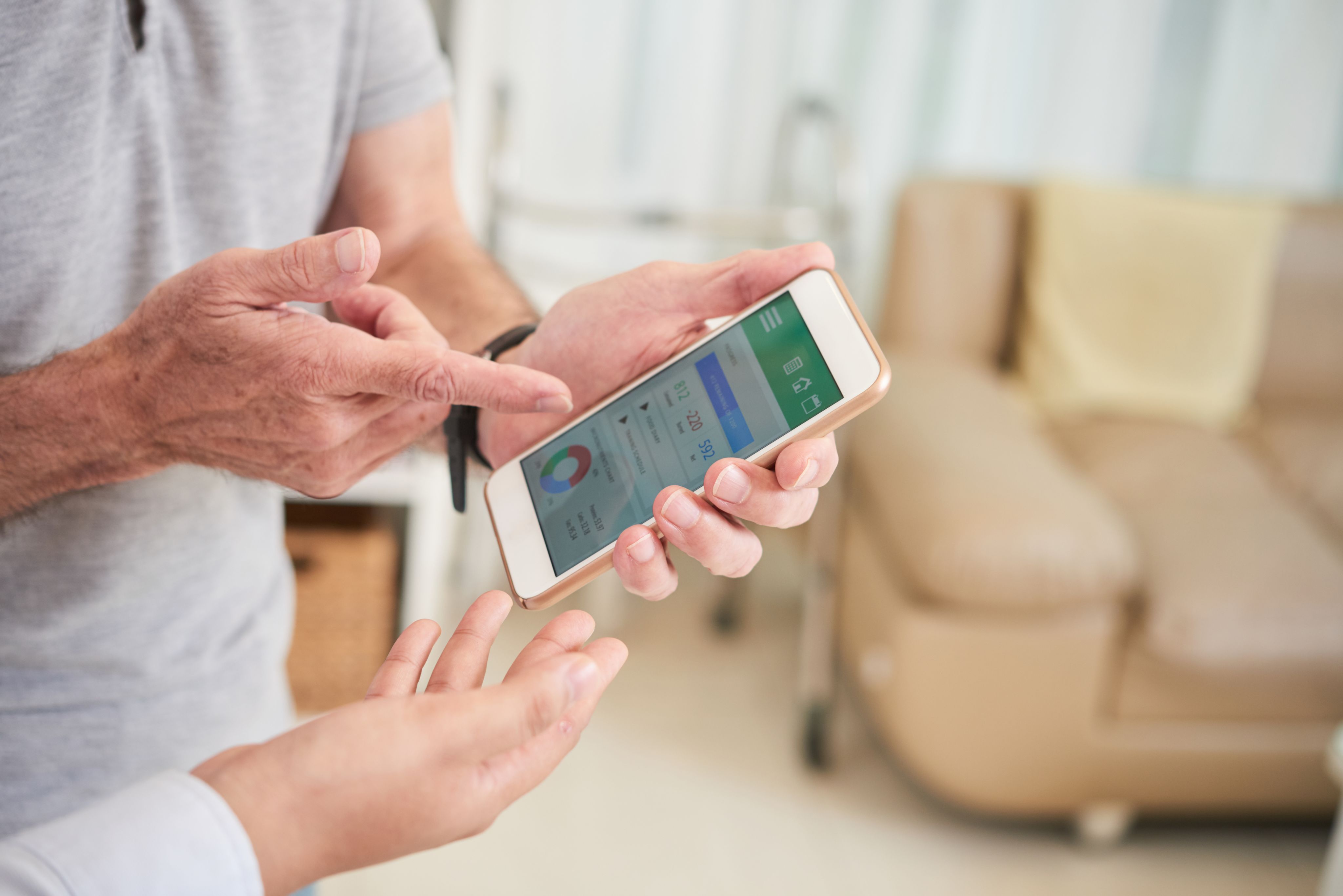 Close-up on the hands of a patient and a clinician looking at a health monitoring app on a smartphone.