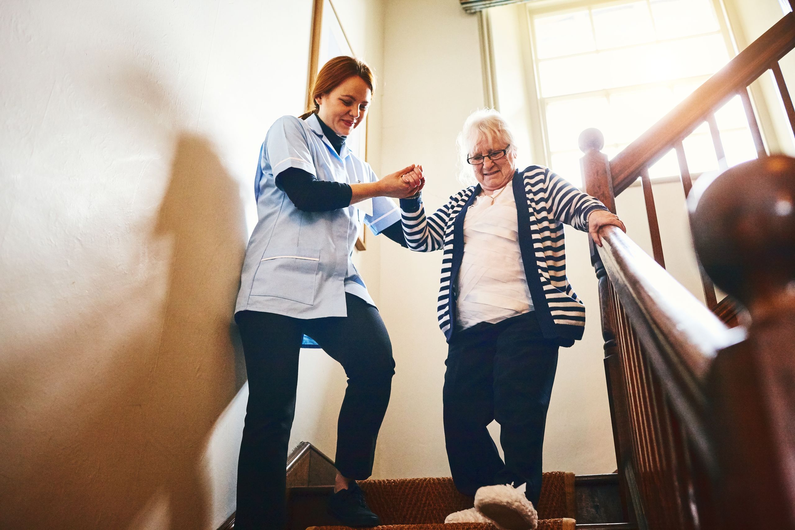 Social care worker helping old woman down the stairs.
